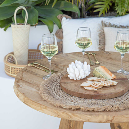 Wooden table with wine glasses, cheese, and crackers on a patio setting.