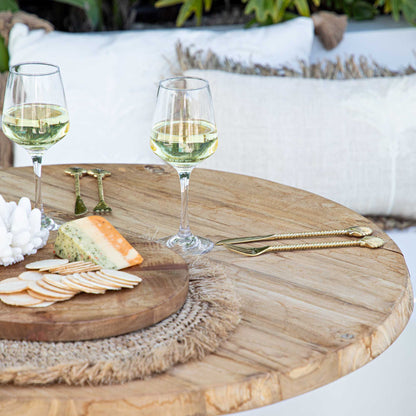 Two glasses of white wine on a wooden table with cheese and crackers, outdoor setting.