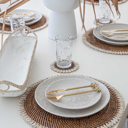 Elegant table setting with white plates, gold cutlery, and woven placemats on a white table.