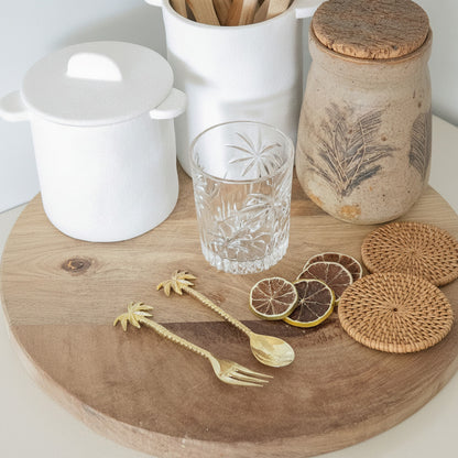 Wooden cutting board with glass, lemons, and kitchen utensils on a white surface