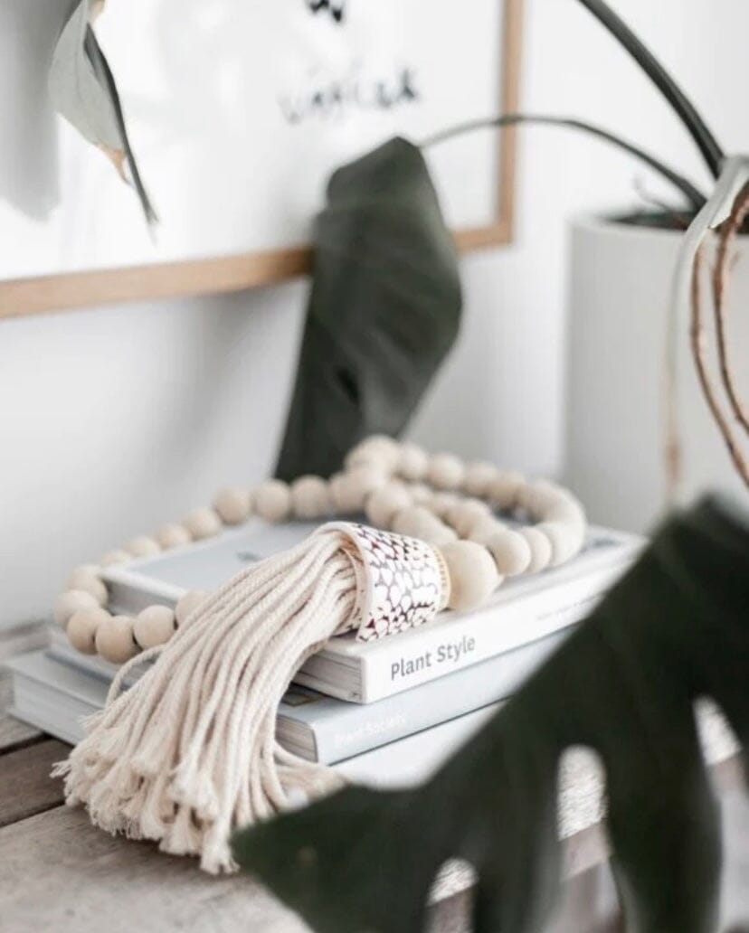 A decorative garland made of natural wooden beads, large tiger shells, and cotton tassels, displayed in a home setting.