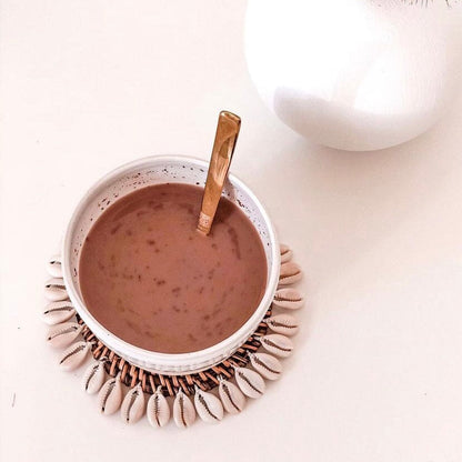 Cup of hot chocolate with a spoon on a decorative coaster on a light surface