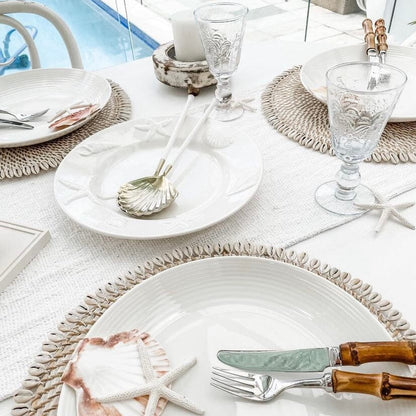 Table setting with white plates, glasses, and silverware on a textured tablecloth.